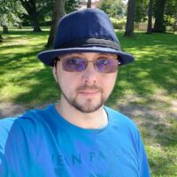 Selfie mit blauem Fedora, blauem Tshirt in einem kleinen Park.