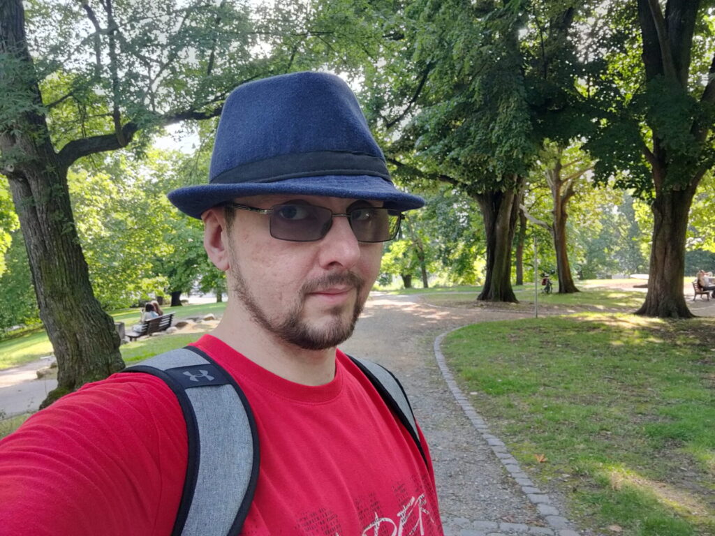 Selfie von mir mit blauem Fedora, rotem T-Shirt und grauem Rucksack